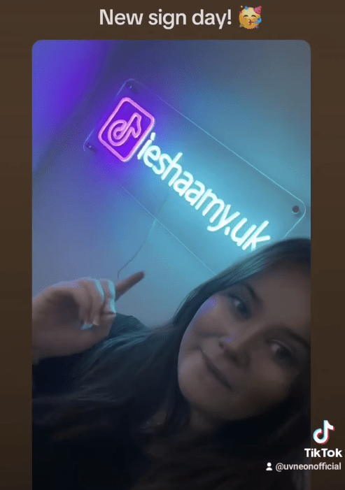 TikTok gaming streamer showing off her custom LED neon sign with username @ieshaamy.uk, featuring the TikTok logo in pink and blue glow.