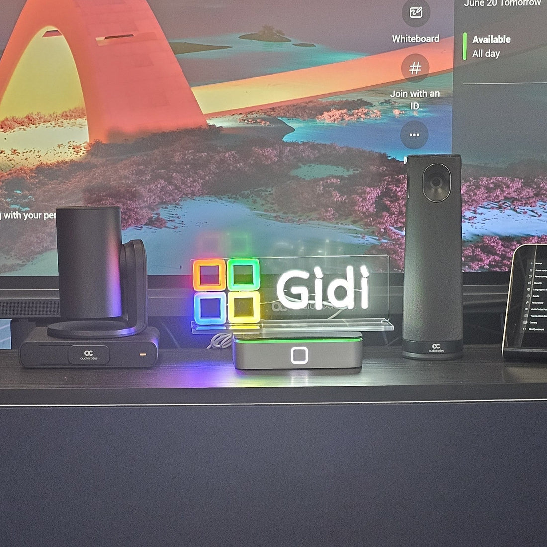 Custom UV Neon LED sign reading "Gidi" displayed at Commsverse as a USB-powered speaker gift, featuring multicoloured LED blocks on an acrylic stand.