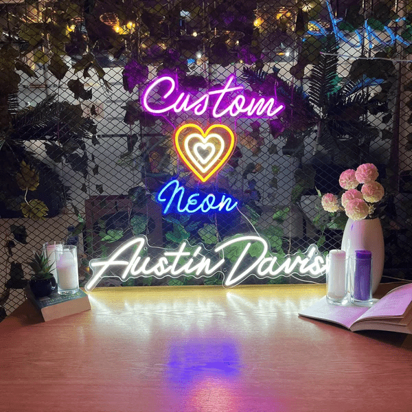 Personalised neon sign with layered heart design and the name 'Austin Davis' in glowing LED lights, displayed in a decorative indoor setting with flowers and candles