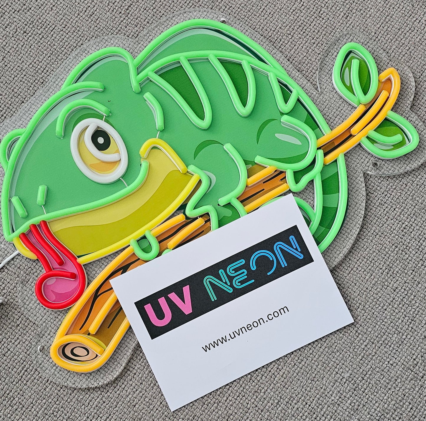 Chameleon lizard UV neon sign switched off – acrylic-backed cartoon reptile design in green and yellow, shown unlit on fabric background
