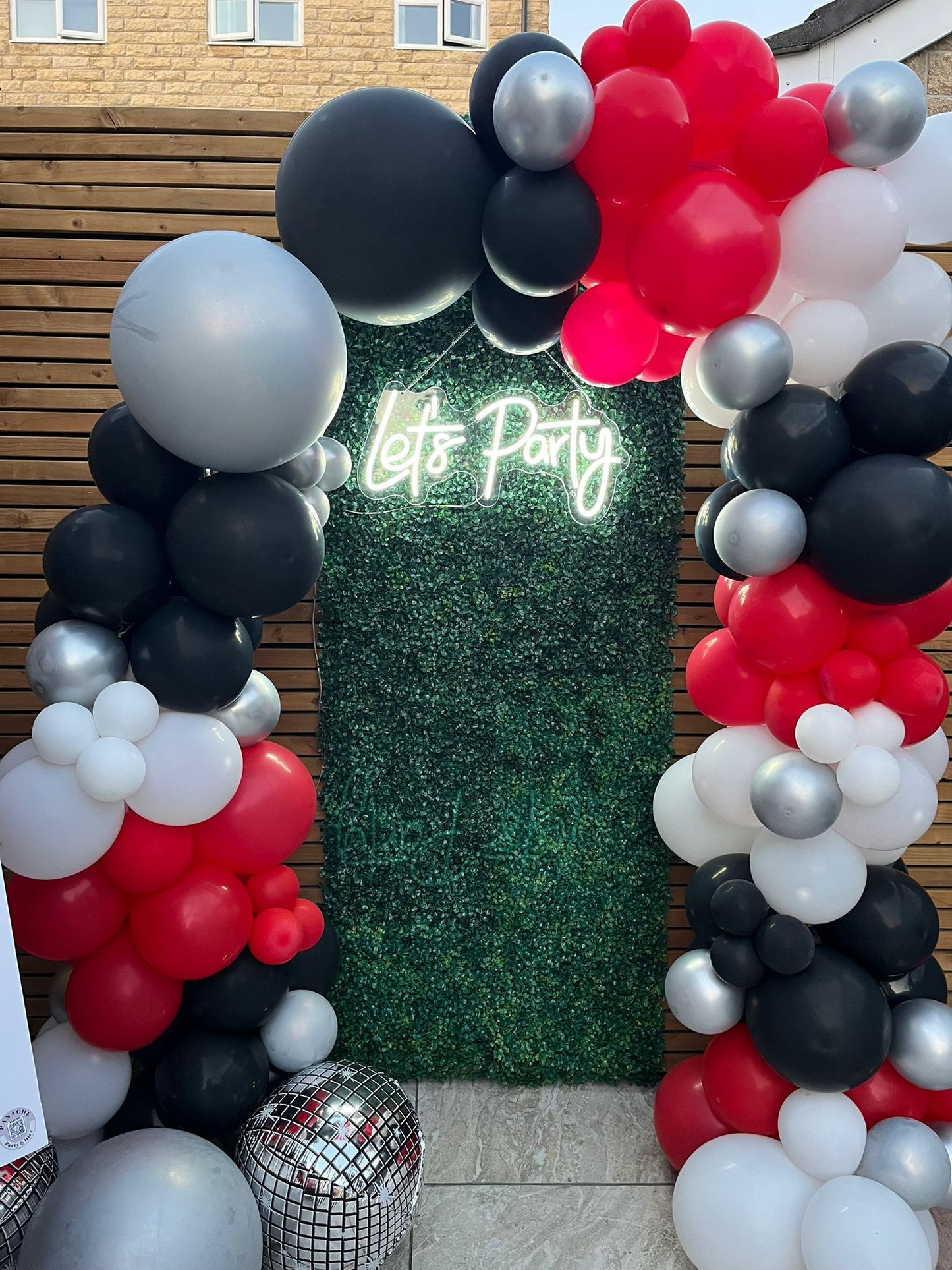 Let's Party LED neon sign on green wall backdrop with red, black, and white balloon arch — perfect for birthdays, events, and celebrations