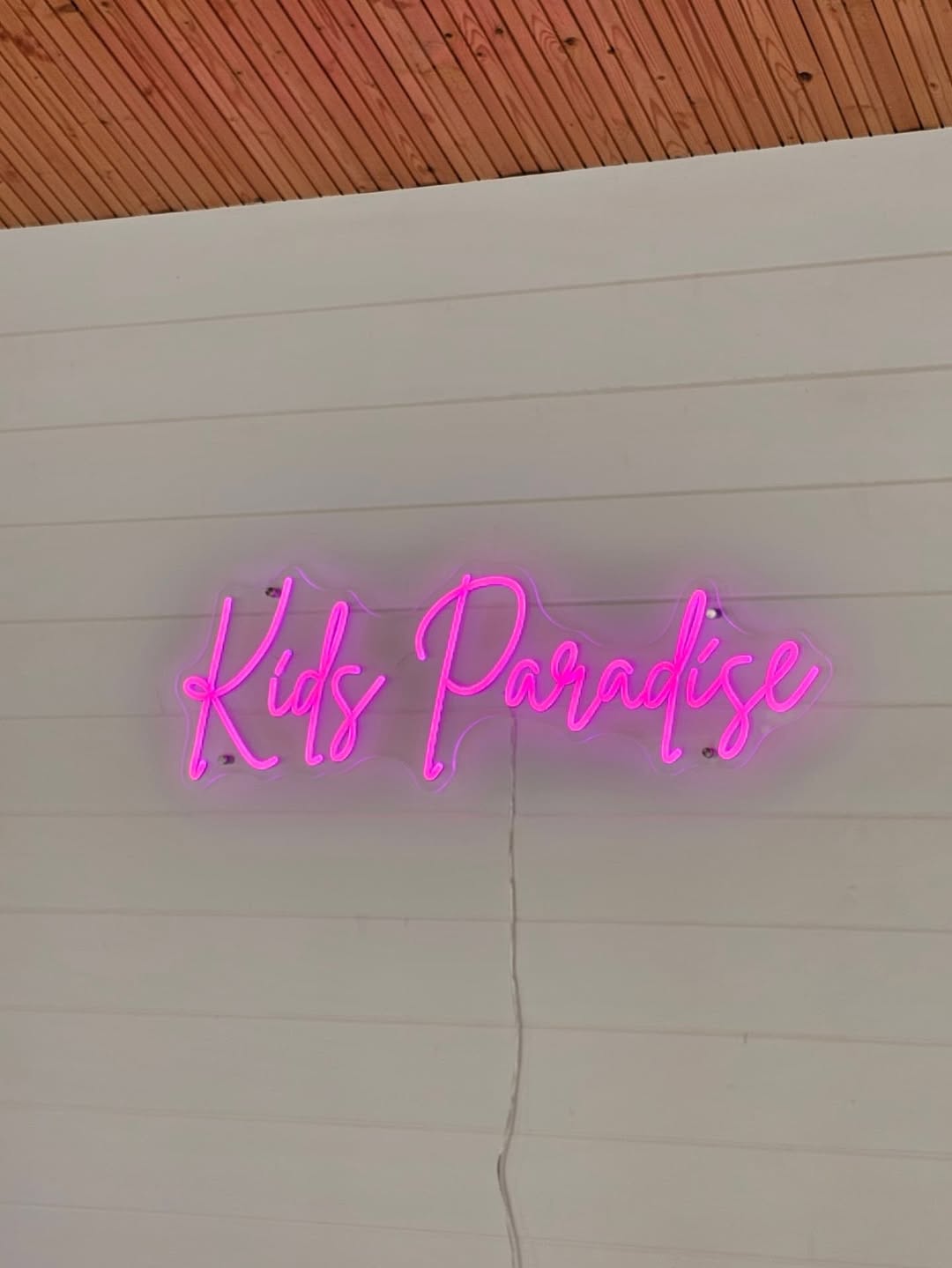 Pink LED neon sign reading Kids Paradise in elegant script font on white shiplap wall, custom children's bedroom neon sign UK