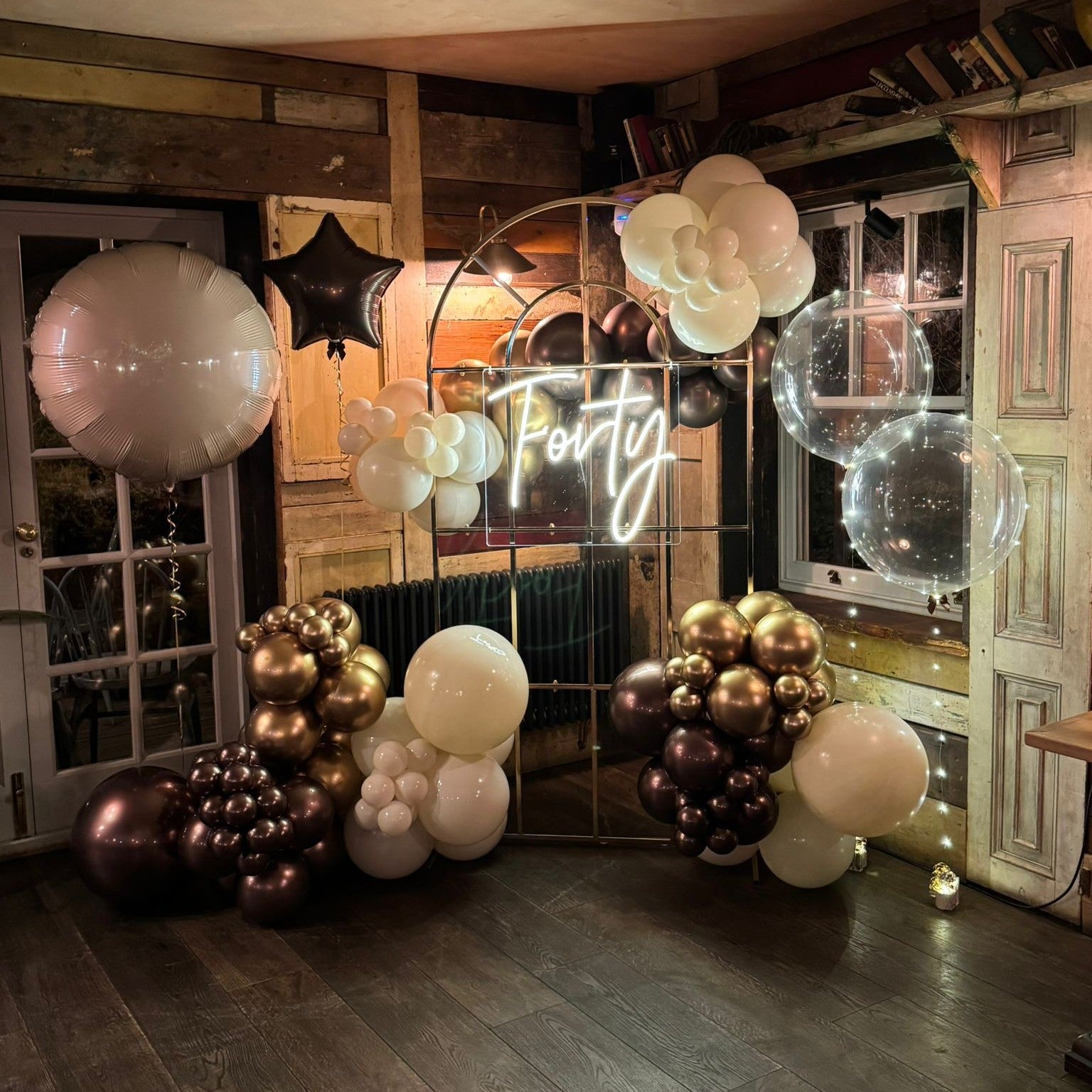 A custom cold white LED neon sign displaying the word "Forty" in a script font, mounted on a clear rectangular acrylic backing. The sign is featured as a centerpiece for a 40th birthday party celebration, styled with a luxury balloon arch and pampas grass decor by a UK event professional.