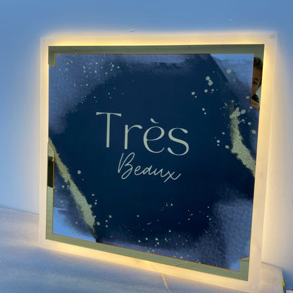 Square backlit acrylic sign with gold and navy printed logo for Très Beaux aesthetics clinic in Worcestershire, LED backlit wall sign