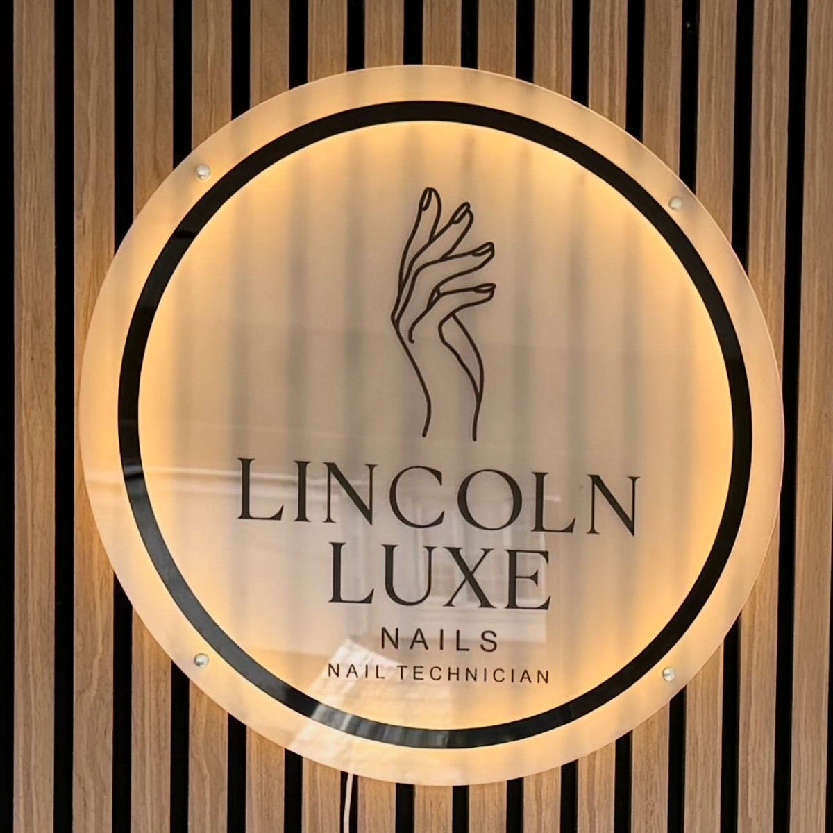 Backlit LED neon sign for Lincoln Luxe Nails beauty salon featuring circular UV-printed logo with warm glow halo effect on slatted wall