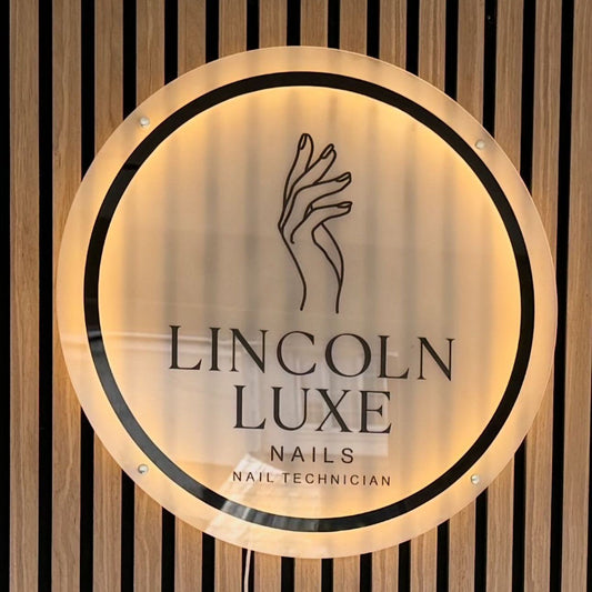 Backlit LED neon sign for Lincoln Luxe Nails beauty salon featuring circular UV-printed logo with warm glow halo effect on slatted wall