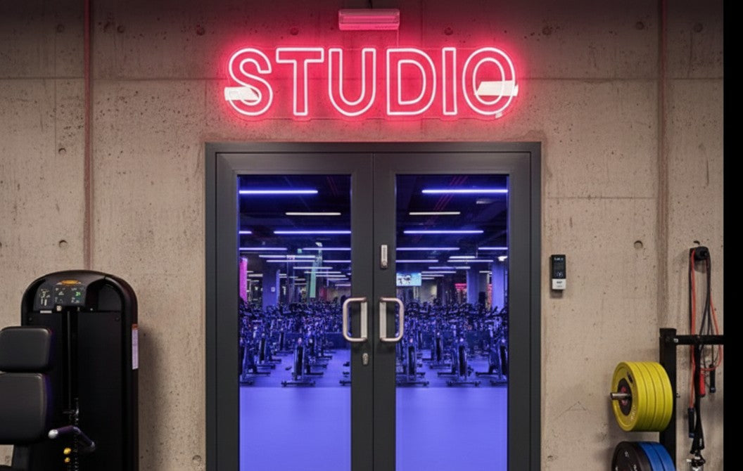 Custom pink neon sign reading STUDIO mounted above modern fitness studio entrance with glass doors and gym equipment visible inside