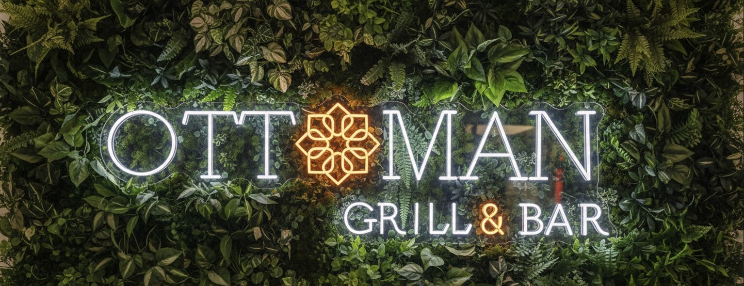 LED neon business sign for Ottoman Grill & Bar restaurant featuring white and orange illuminated logo on lush green living wall backdrop