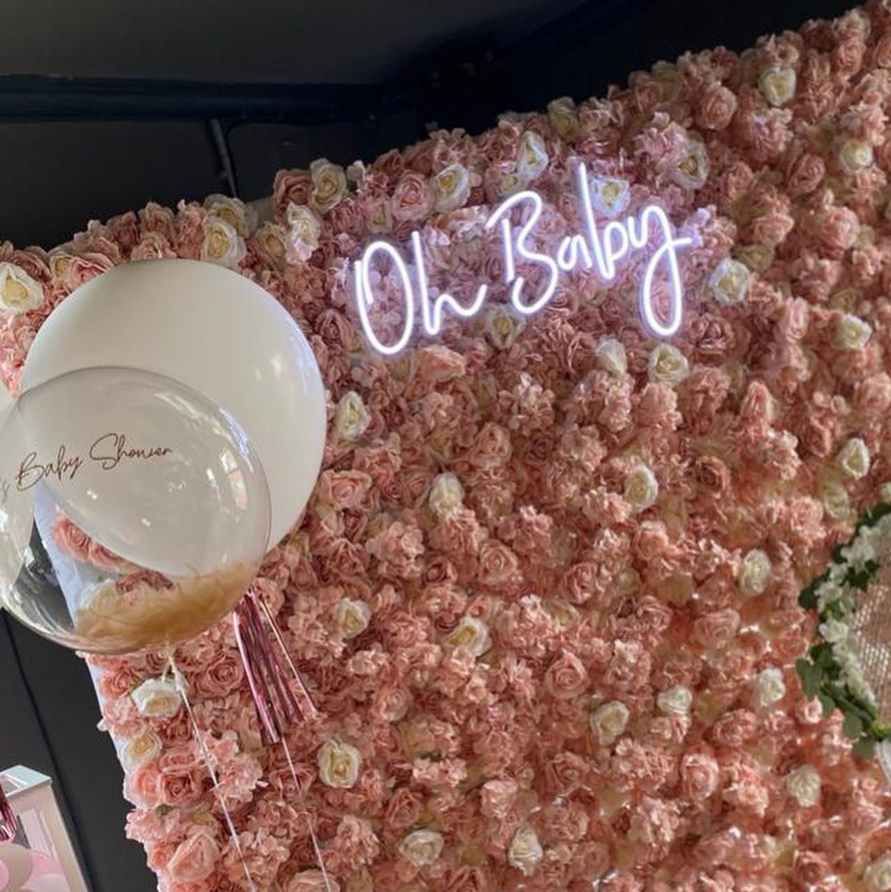 Script "Oh Baby" neon light mounted on a lush pink and white rose flower wall backdrop, perfect for a girl's baby shower or garden-themed event.