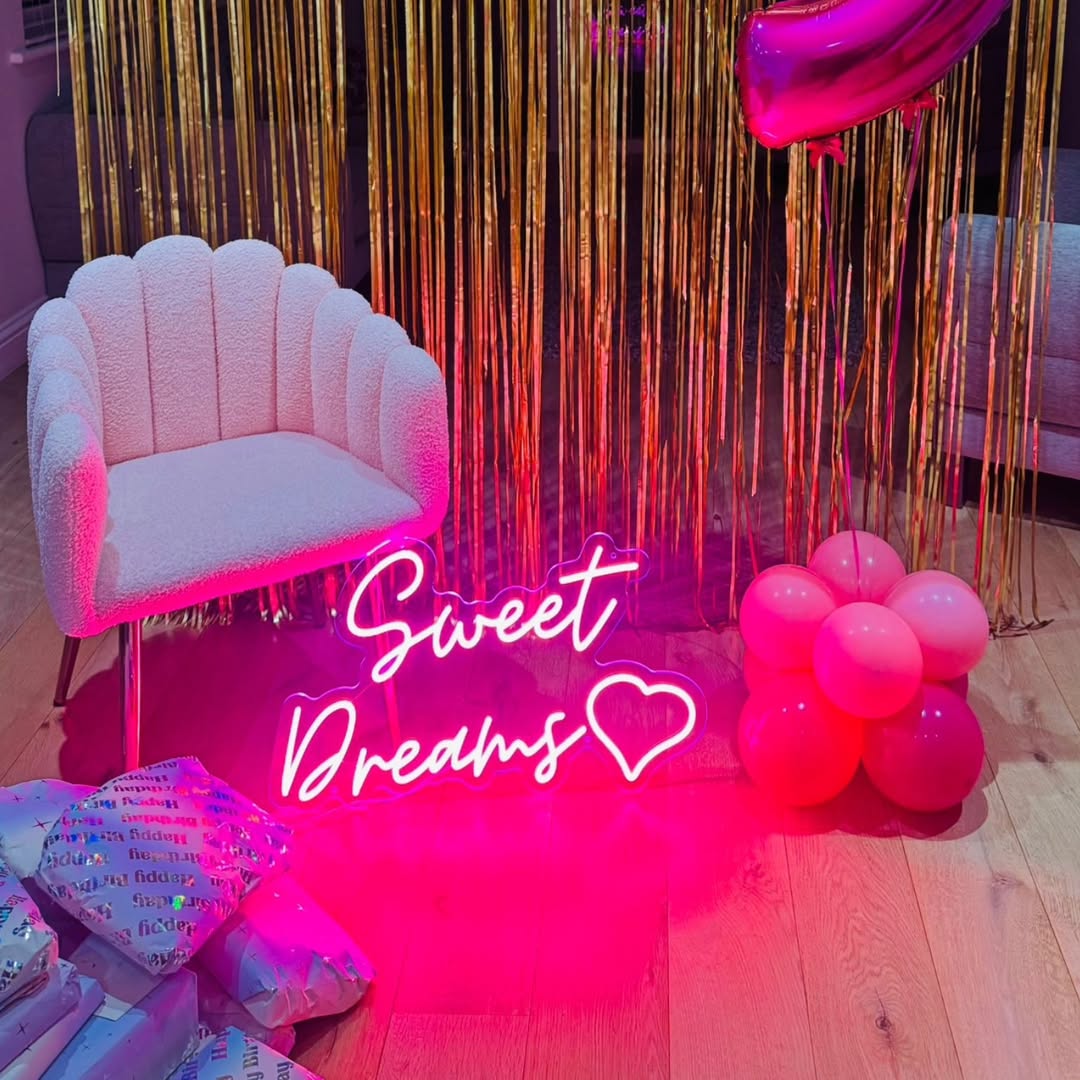 Pink LED neon sign Sweet Dreams with heart icon on party backdrop with gold curtain, pink balloons and velvet chair, bedroom event décor UK