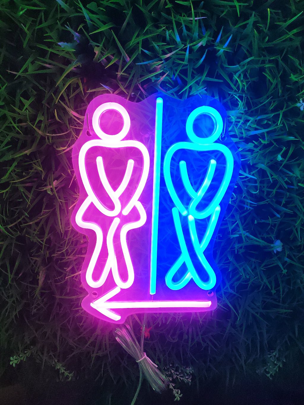Toilet neon sign illuminated showing pink and blue crossed legs figures with directional arrow for bathroom wayfinding